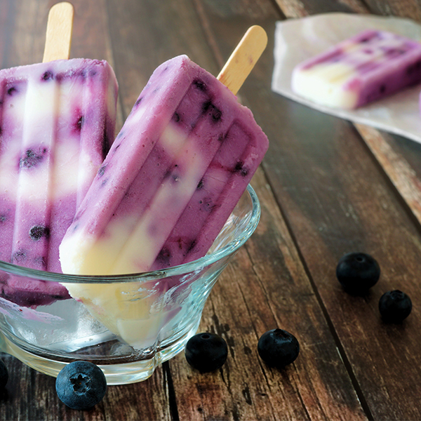 Homemade blueberry vanilla popsicles in a bowl clear bowl against a rustic wood background